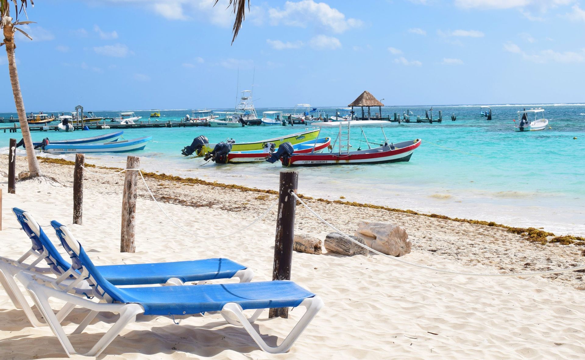 Beach with turquoise water, boats, and lounge chairs under a clear blue sky.