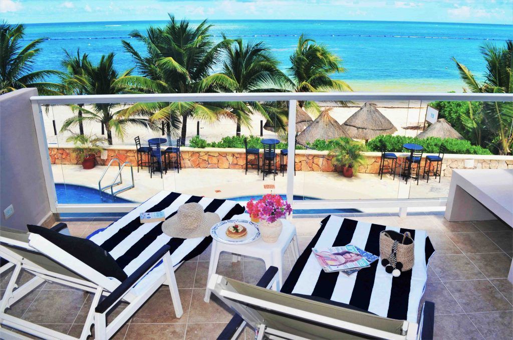 Balcony view of ocean, beach, and palm trees with lounge chairs, snacks, and pool.