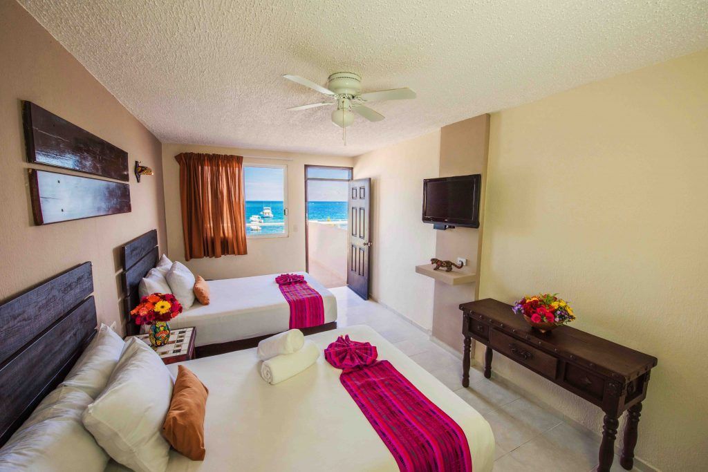 Hotel room with two beds, ocean view, TV, dark wood furniture, and colorful accents.