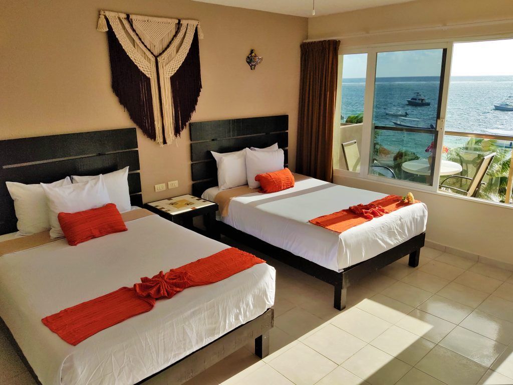 Hotel room with two beds, orange accents, and a view of the ocean.