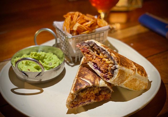 Burrito cut in half, with guacamole and fries on a plate.