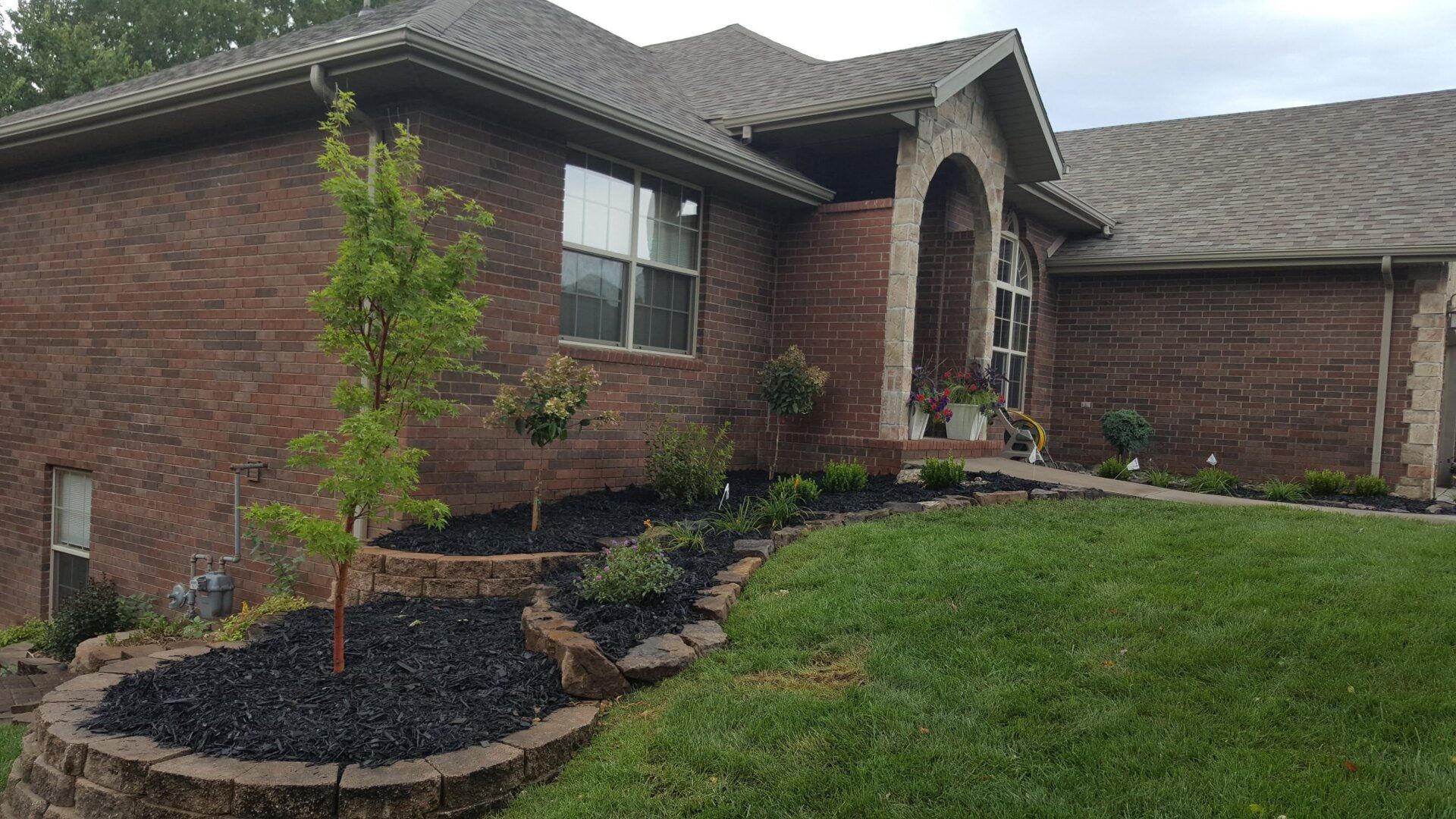 Brick house with landscaped yard and black mulch beds.