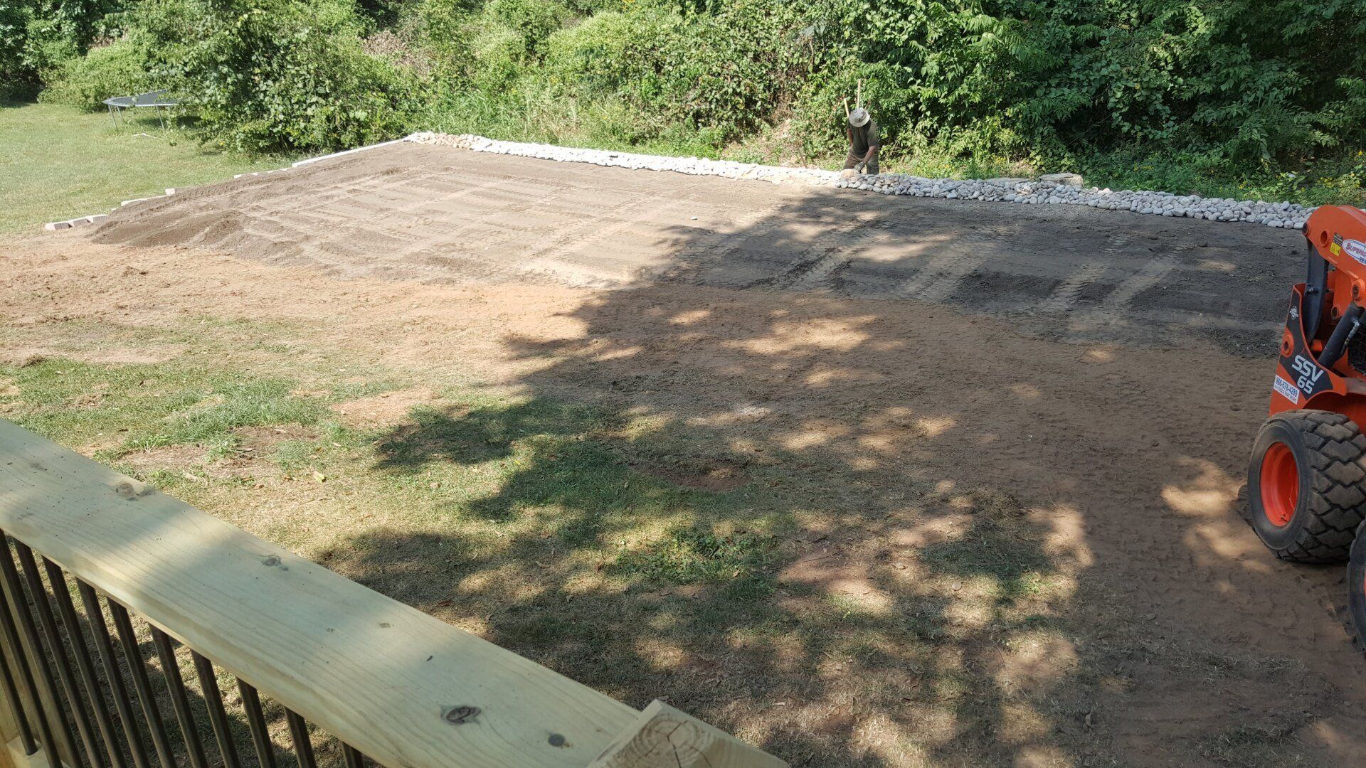 Gravel and dirt area, bordered by rocks, prepared for landscaping next to a deck with an orange tractor.