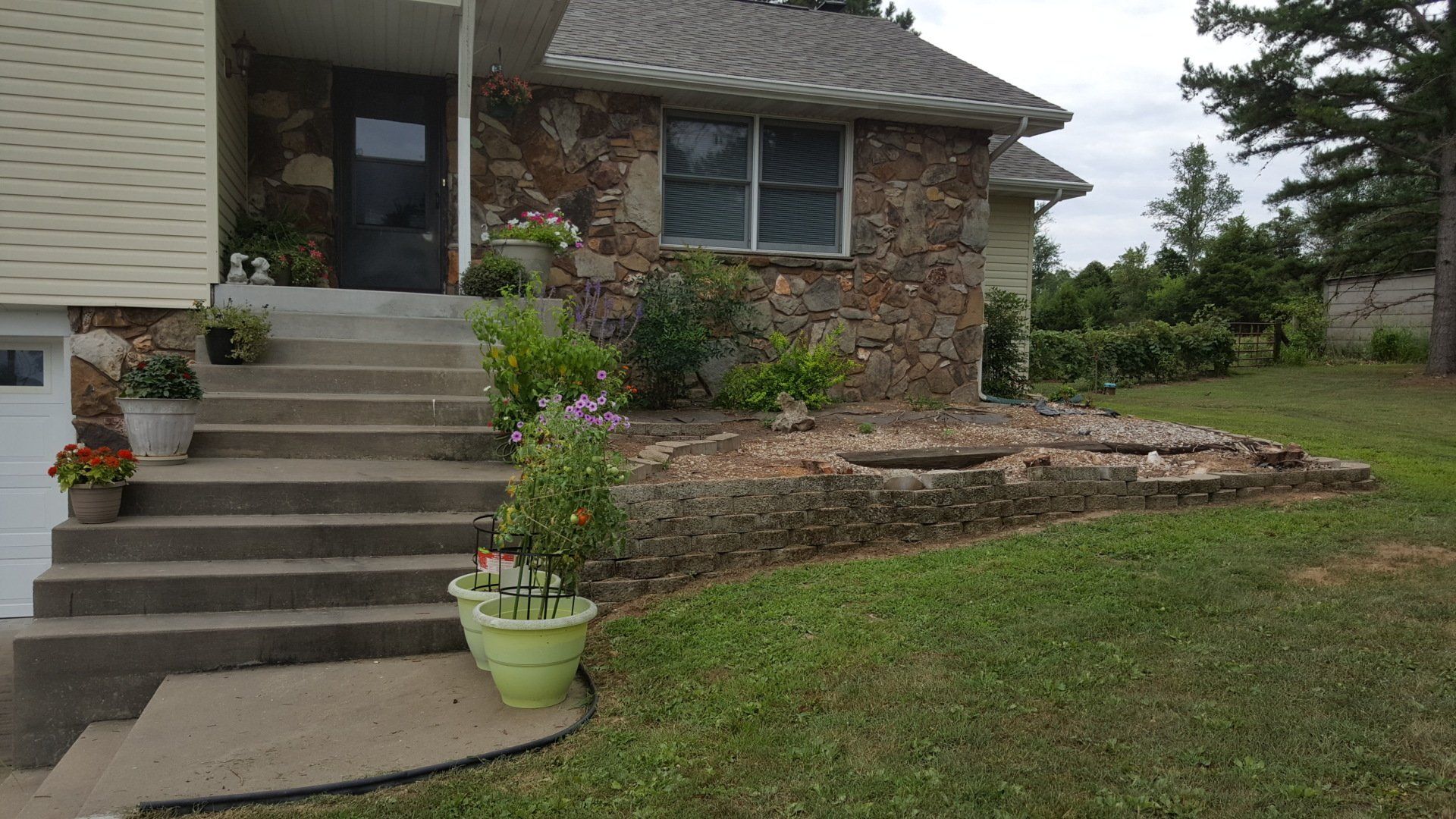 Stone house with concrete steps, potted plants, and small garden bed.