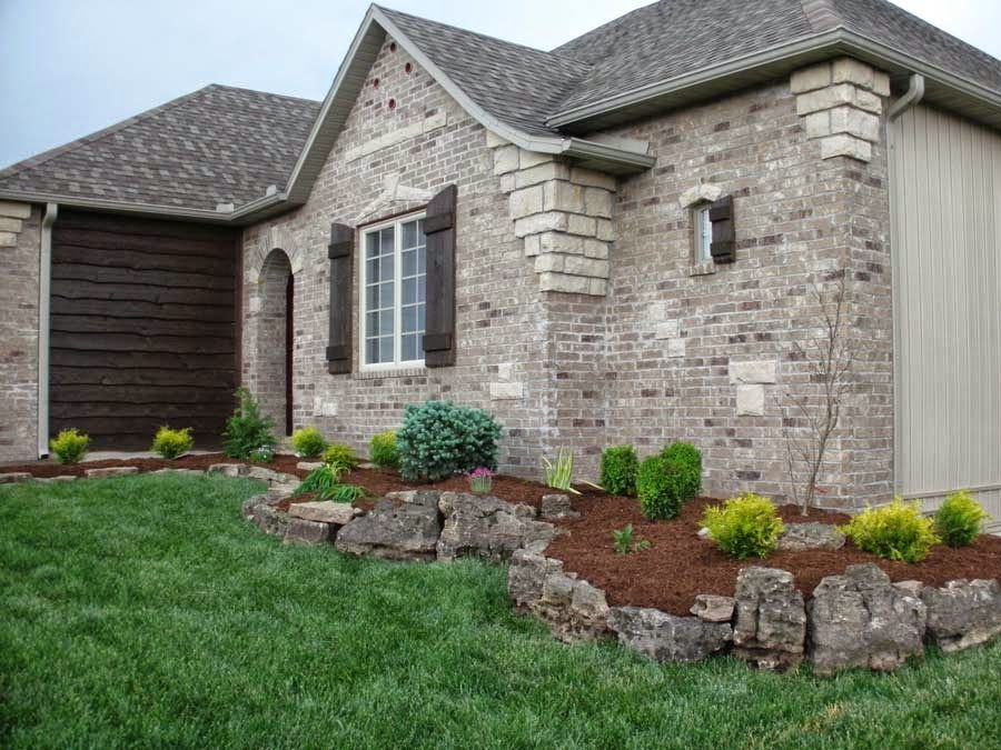 Brick house with landscaped yard, brown shutters, and garage door.
