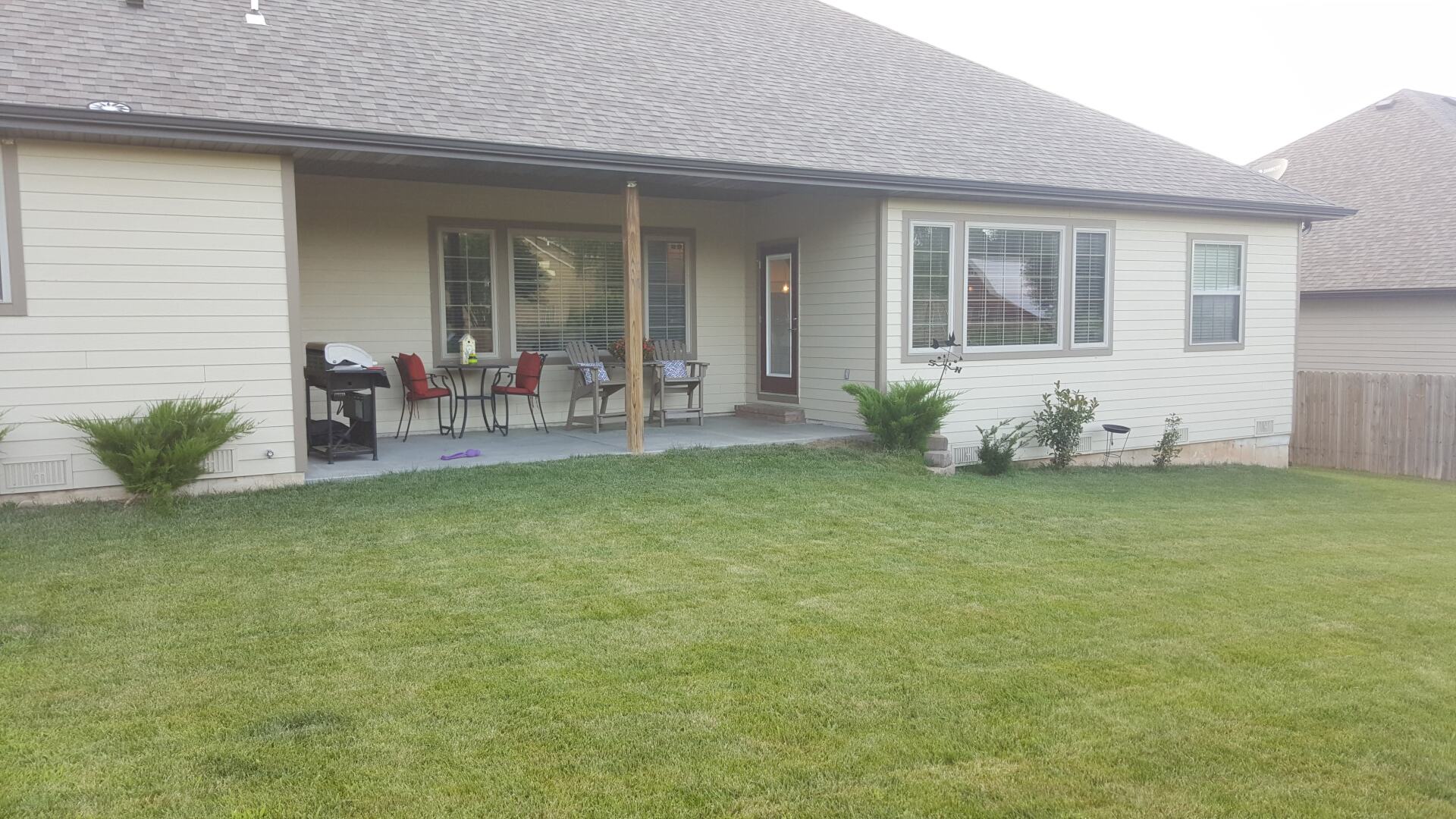Backyard of a beige house with a covered patio, grass, and a grill.