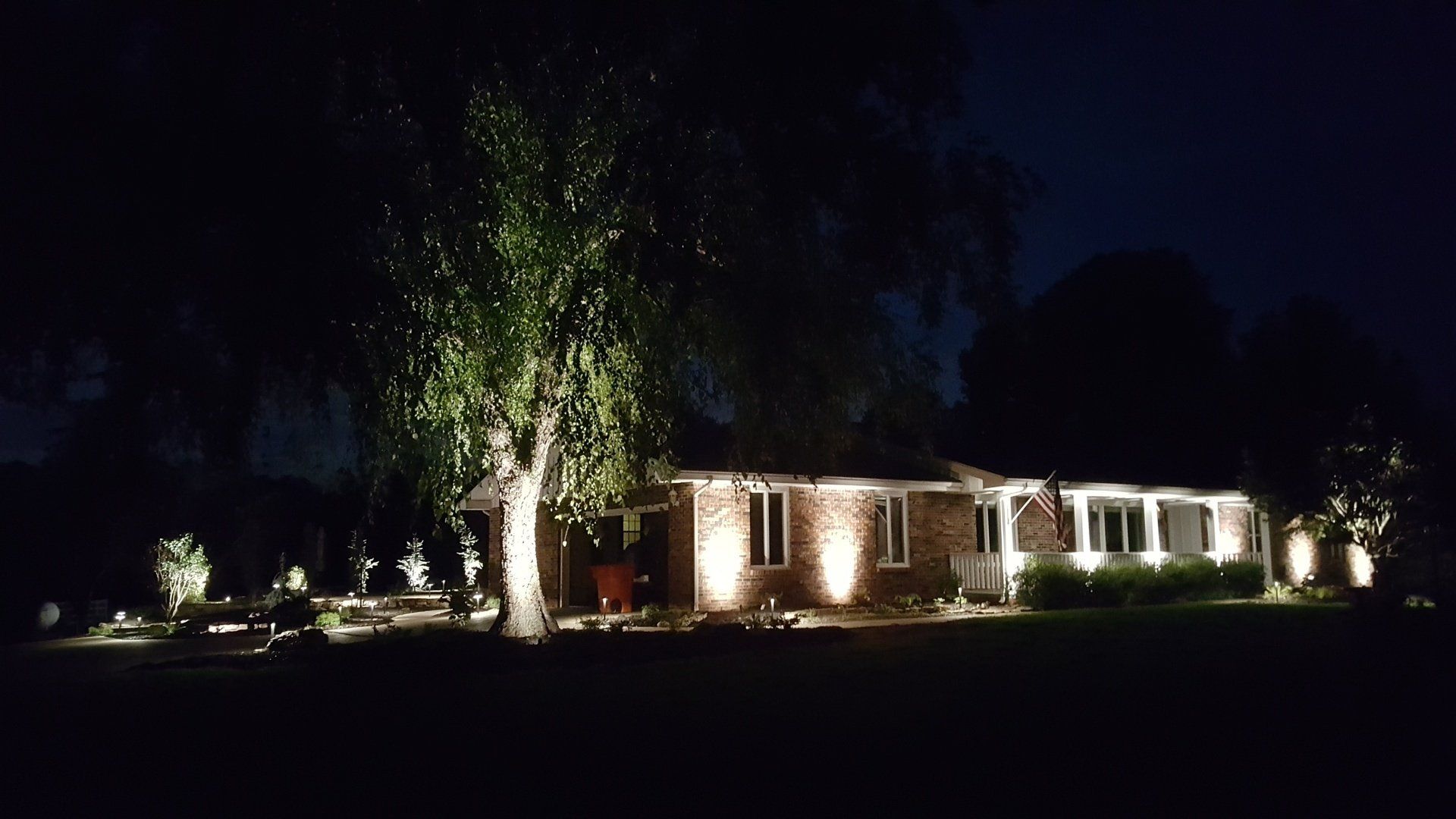 Night view of a house with landscape lighting illuminating the structure and a tree.