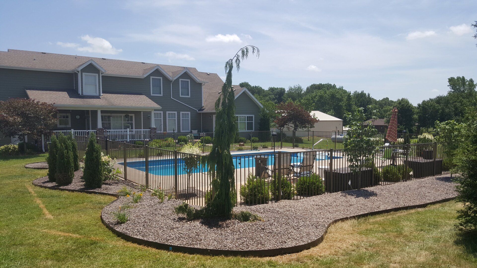 Backyard pool with a house in the background on a sunny day. A decorative fence surrounds the pool.