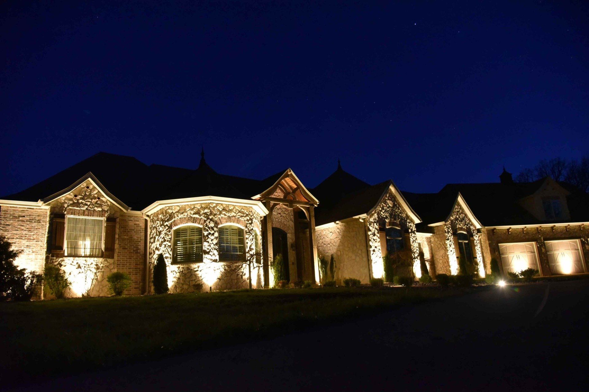Night view of a stone house lit up with outdoor lights against a dark blue sky.