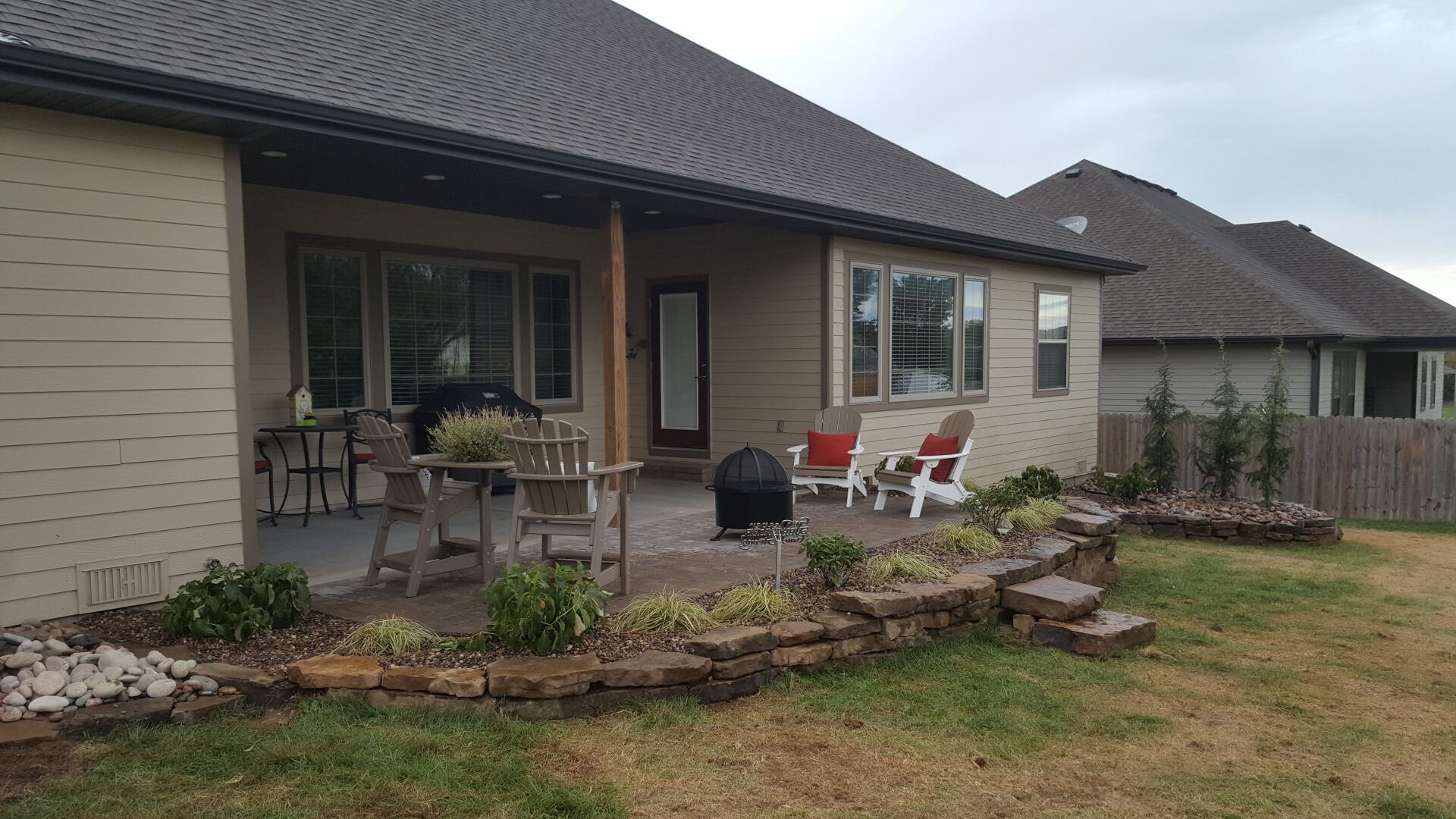 Backyard patio with raised garden bed, stone patio, chairs, and house.