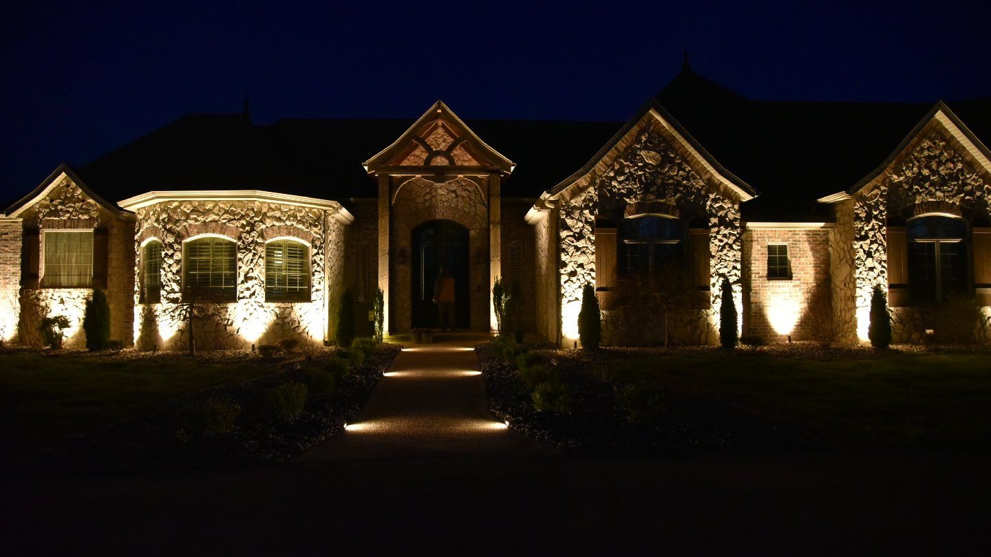 Large house exterior illuminated at night, pathway lit, architectural details highlighted by spotlights.