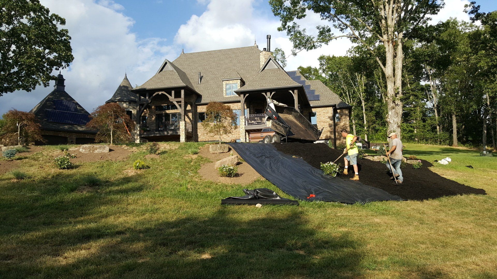 A person raking debris next to a large house with unique architecture, on a sunny day.