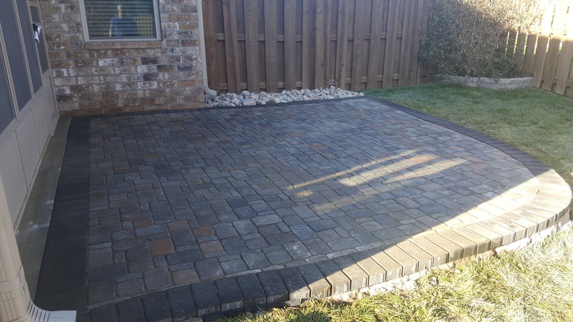 Brick patio in a backyard setting, next to a brick wall and wooden fence.