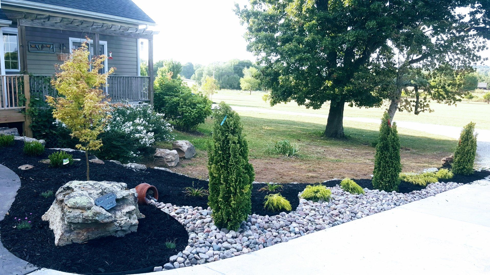 Landscaped yard with a house, various plants, mulch, and stone.