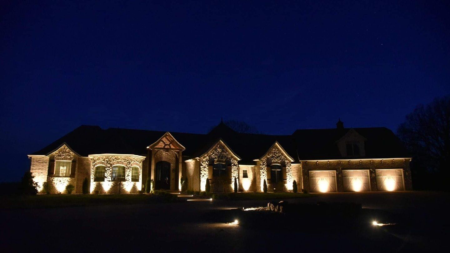 Large house lit up at night, with spotlights highlighting the exterior stone and architecture against a dark blue sky.