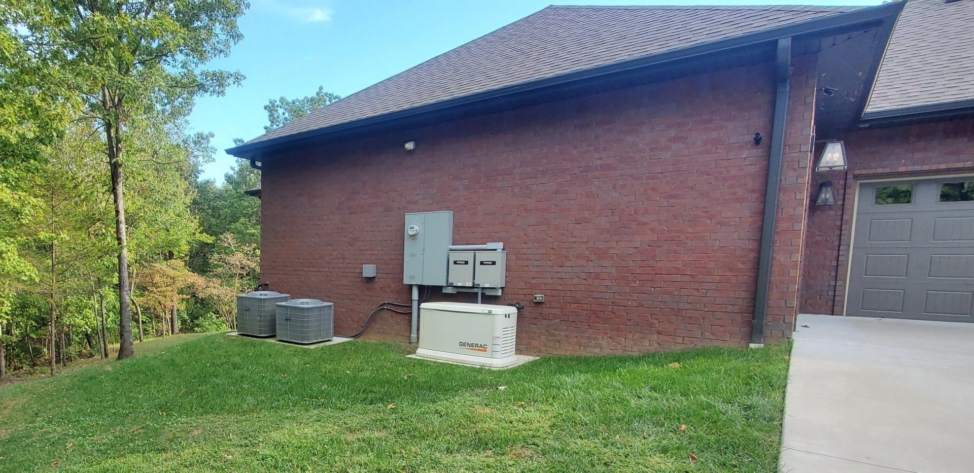 Red brick house with power units and air conditioning units on the side, green grass and blue sky.