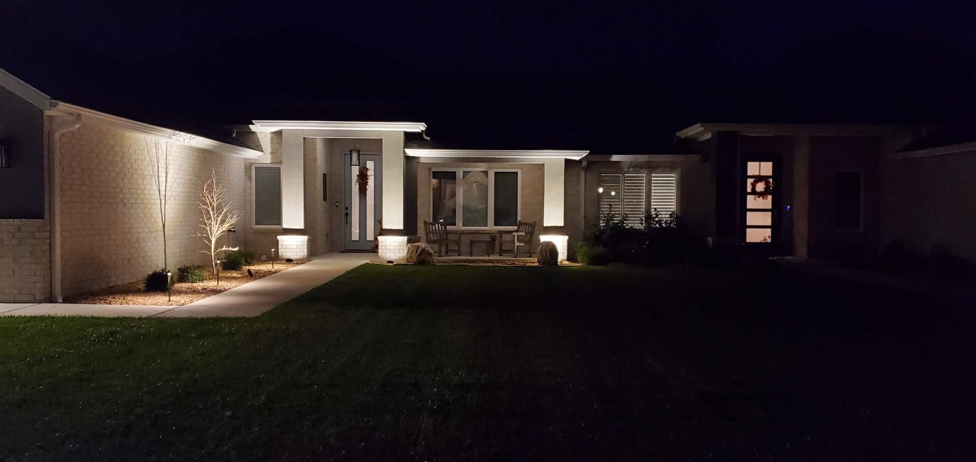 Exterior night shot of a modern home with outdoor lighting illuminating the facade and landscaping.