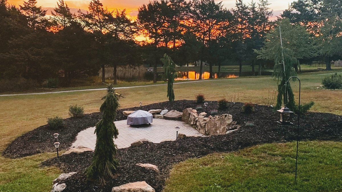 A landscaped backyard with a fire pit, trees, and sunset.