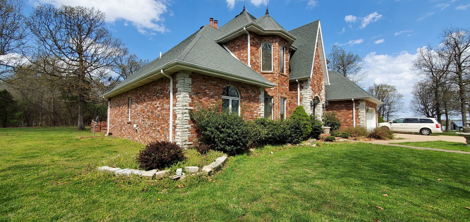 Brick house with a green roof, on a grassy lawn with trees in the background, bright blue sky.