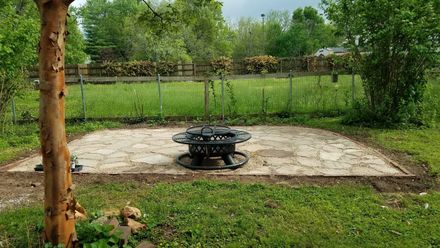 Backyard fire pit area with a fire ring on a gravel base, bordered by wood.