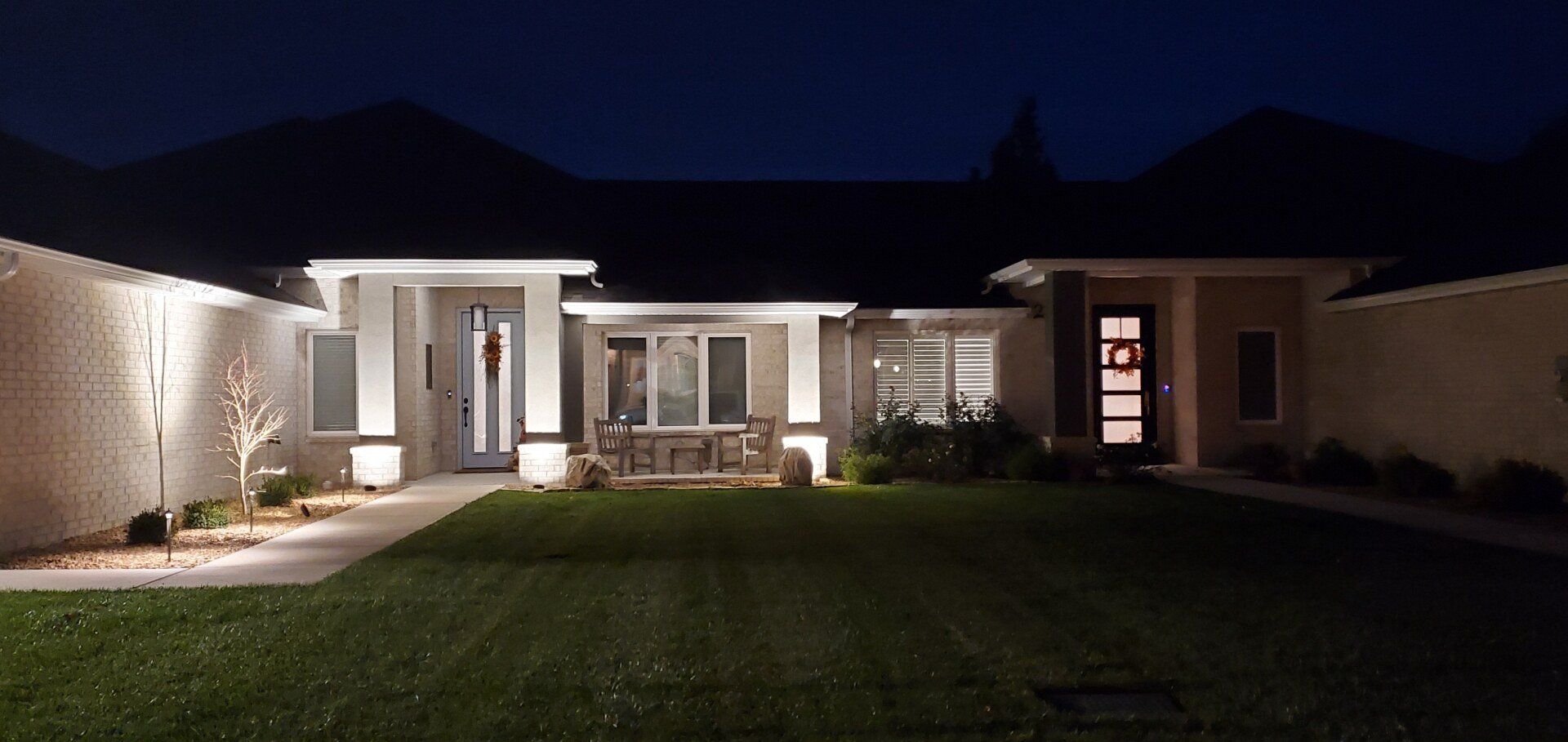 A house at night with the front door and landscaping illuminated by lights. Dark sky.