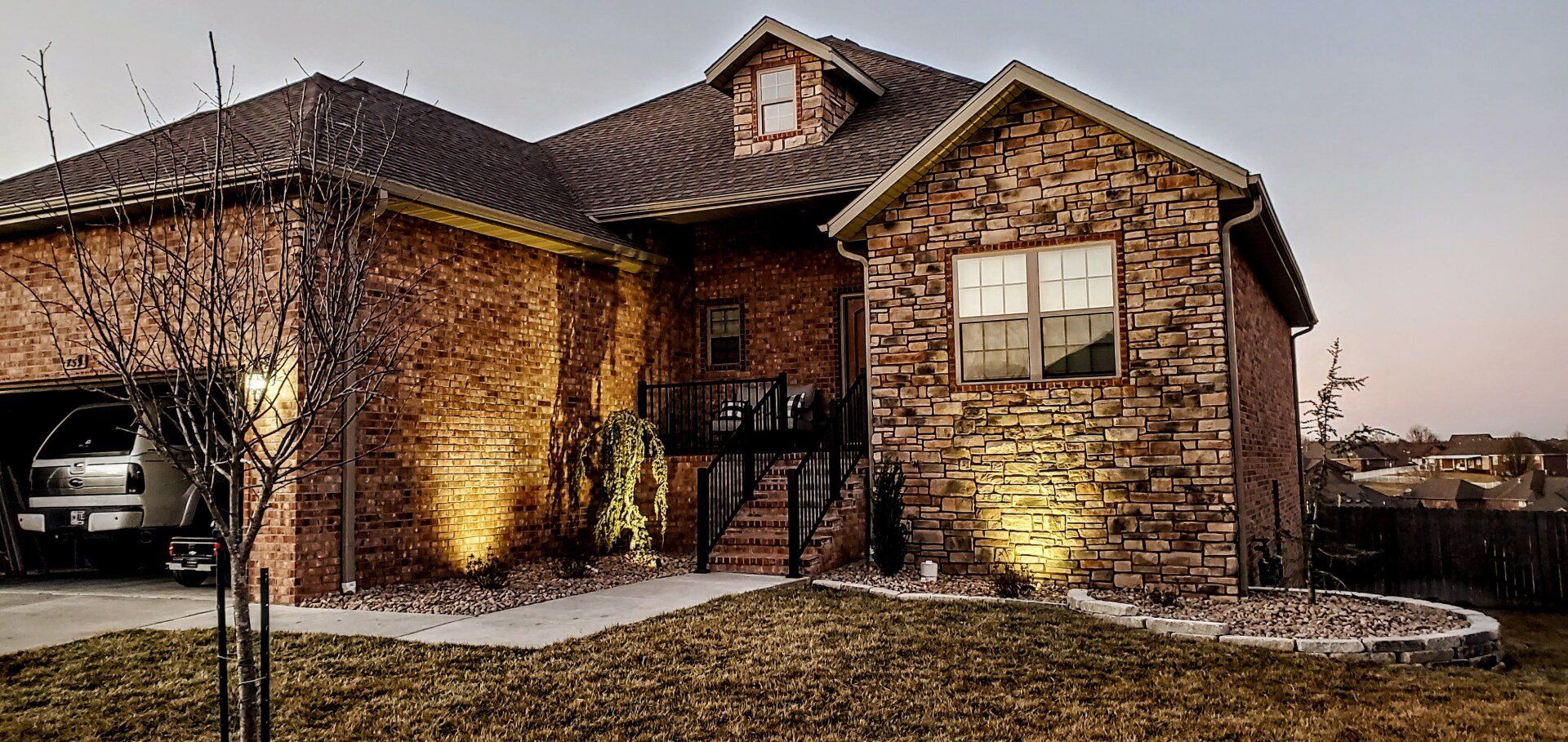 Brick house with illuminated front, includes a garage with a vehicle inside, and a front yard.
