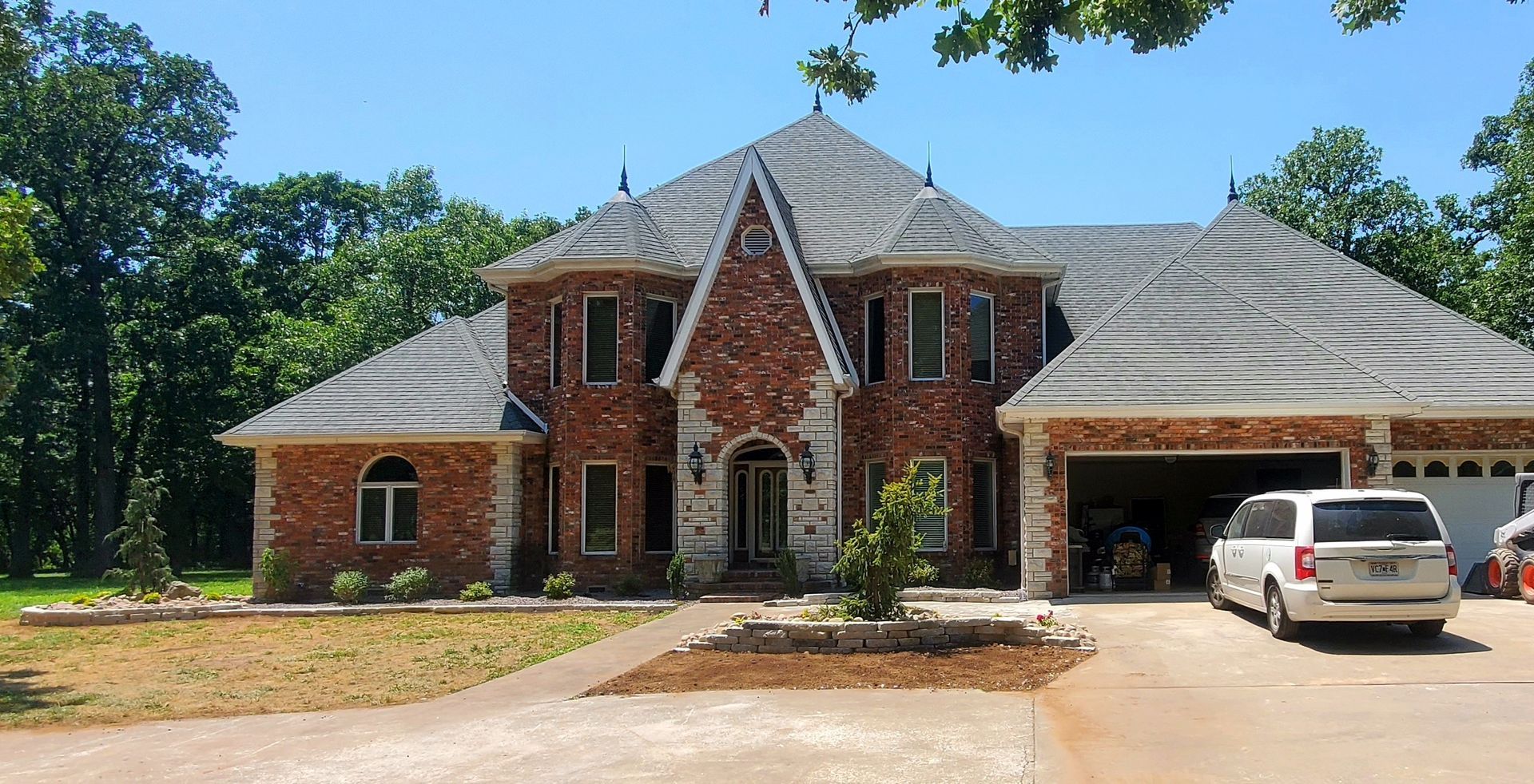 Two-story brick house with gray roof, arched front entry, and attached garage. Sunny day.