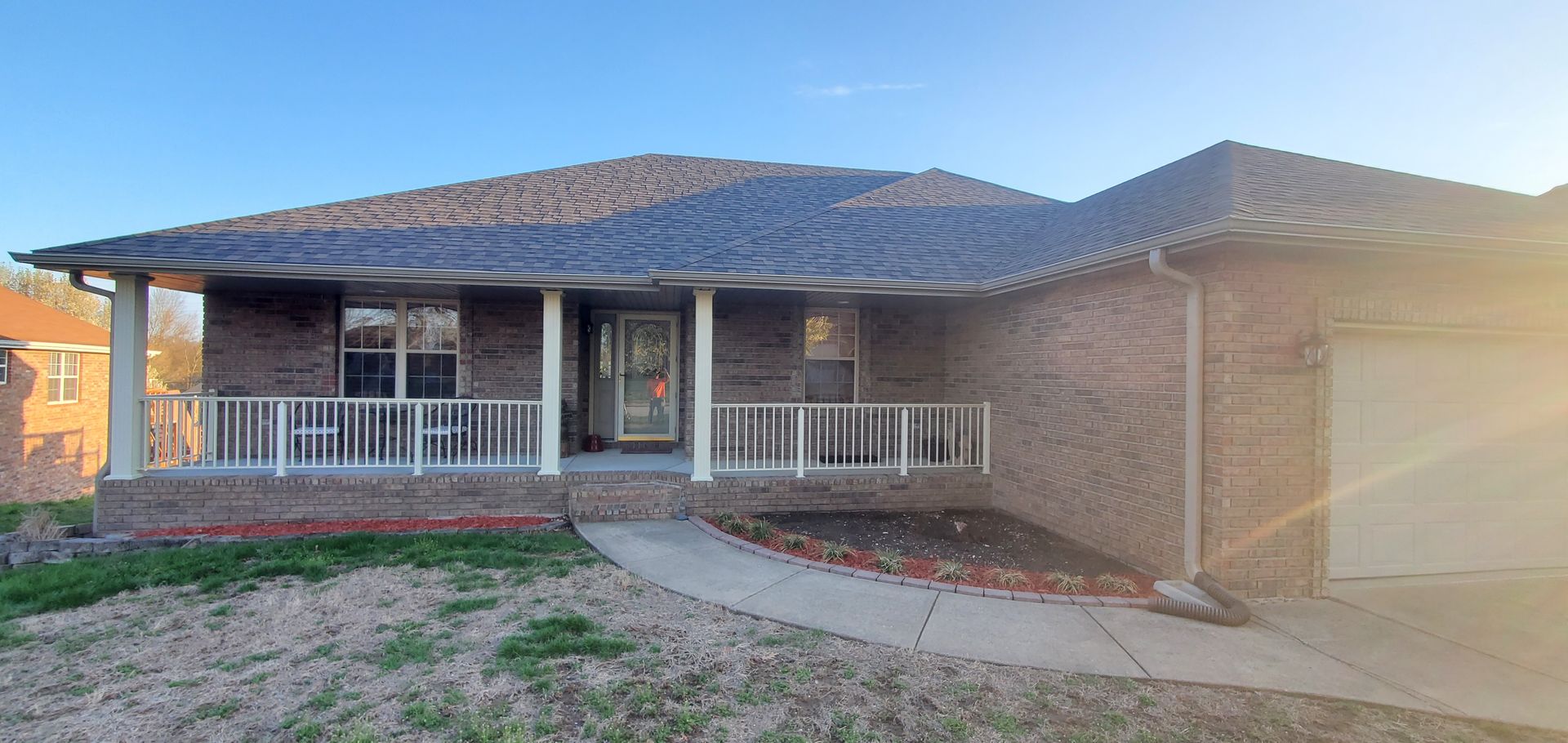 Brick house with a porch and a driveway on a sunny day.