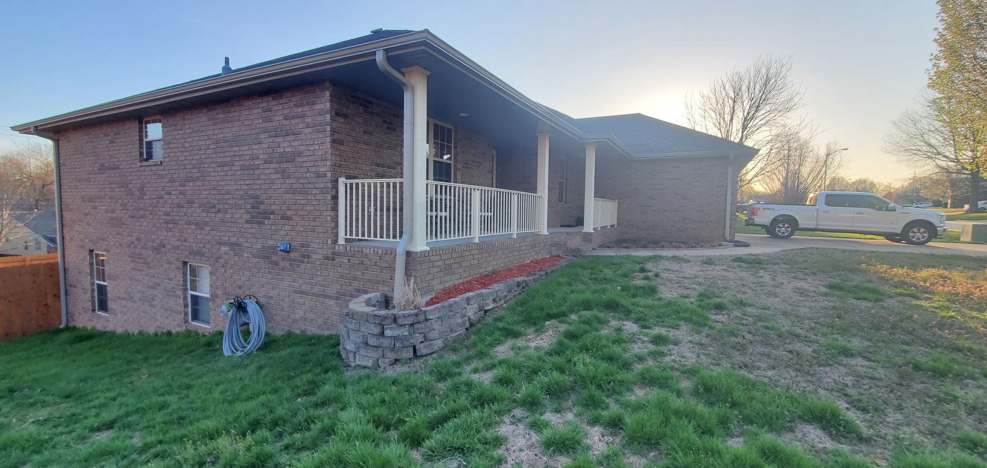 Brick house with a porch and a truck parked nearby on a grassy lawn.