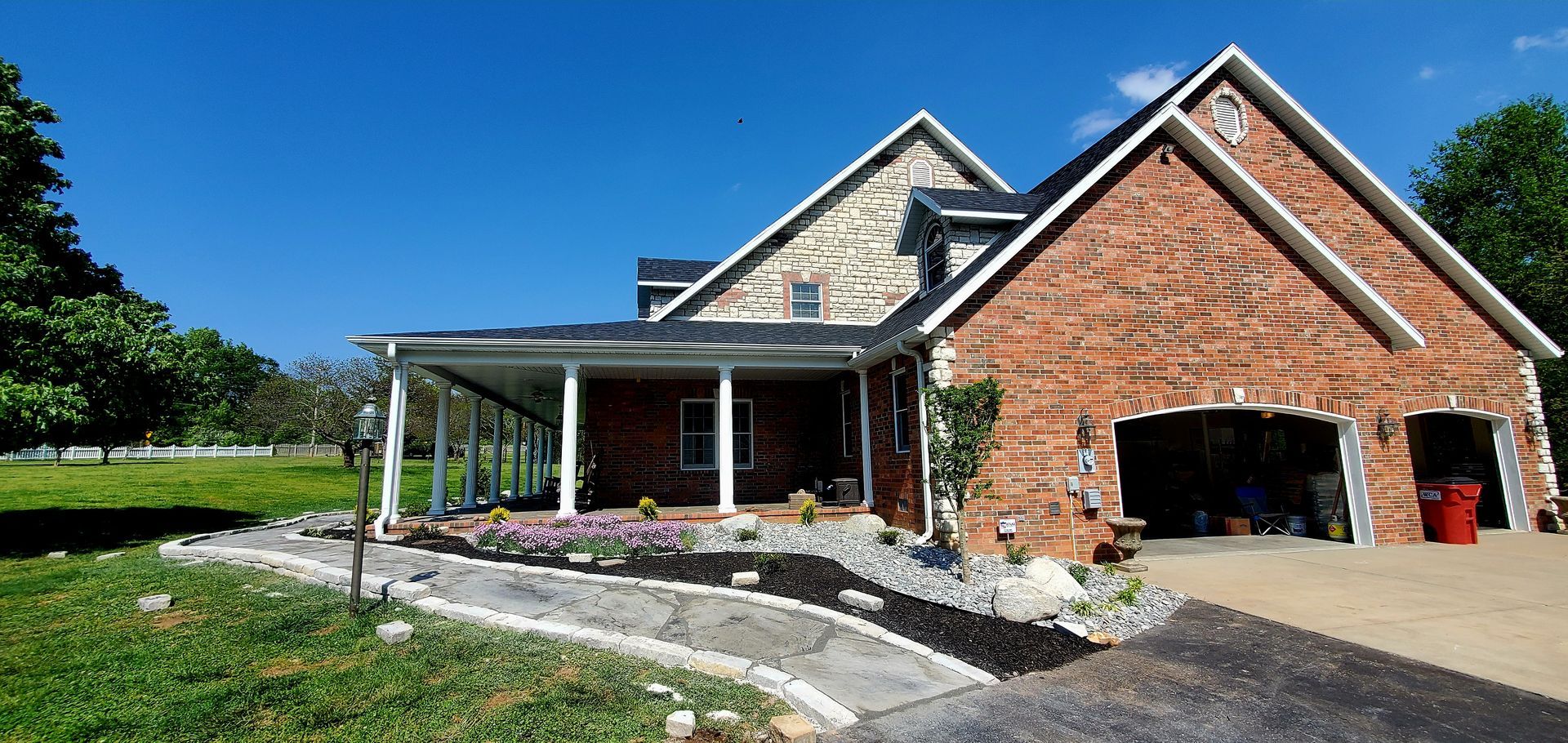 A two-story brick and stone house with a garage and covered porch under a blue sky.