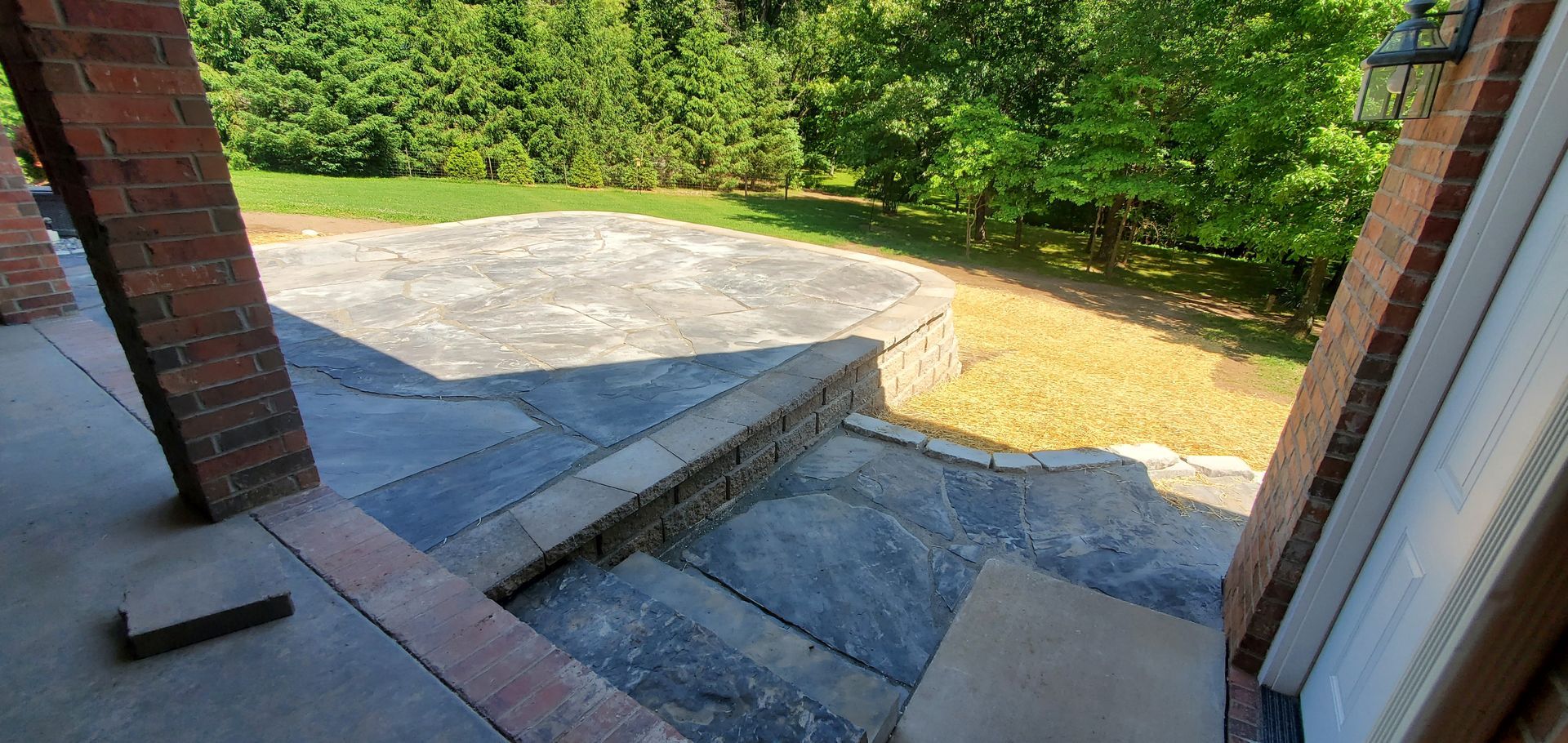 Exterior view with brick pillars, stone steps, and a patio overlooking a yard with trees.
