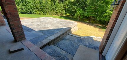 Exterior view with brick pillars, stone steps, and a patio overlooking a yard with trees.