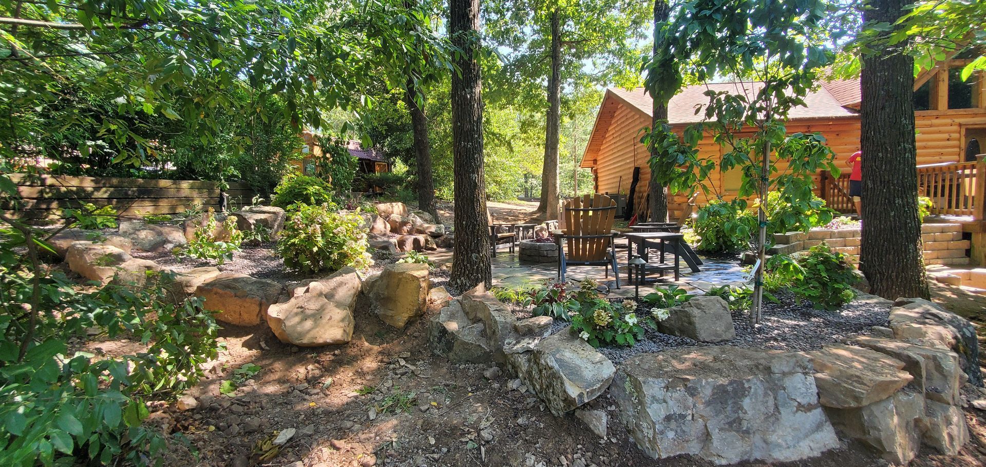 A wood cabin with a rock garden and outdoor seating surrounded by trees.