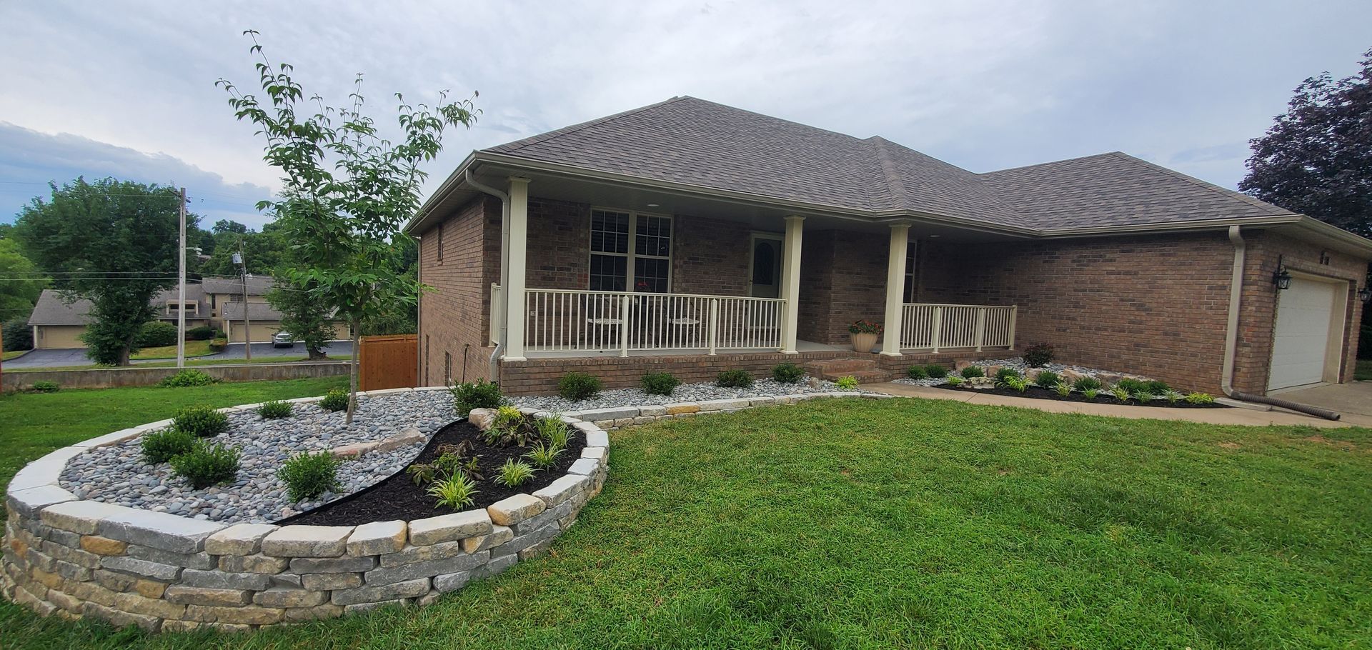 A brick house with a front porch and a landscaped garden bed in the front yard.