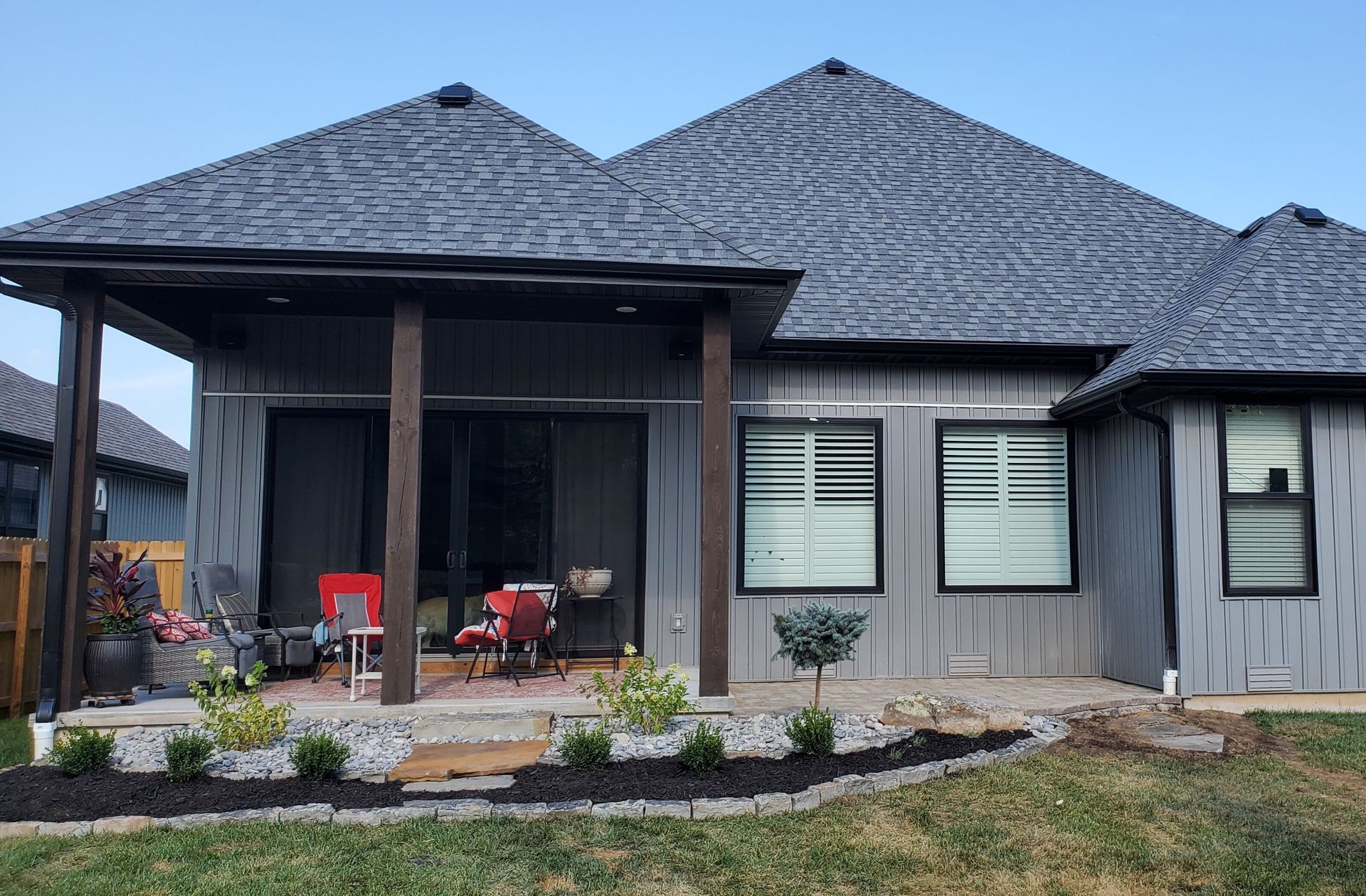 Backyard patio with dark gray roof, gray siding, and a small garden.