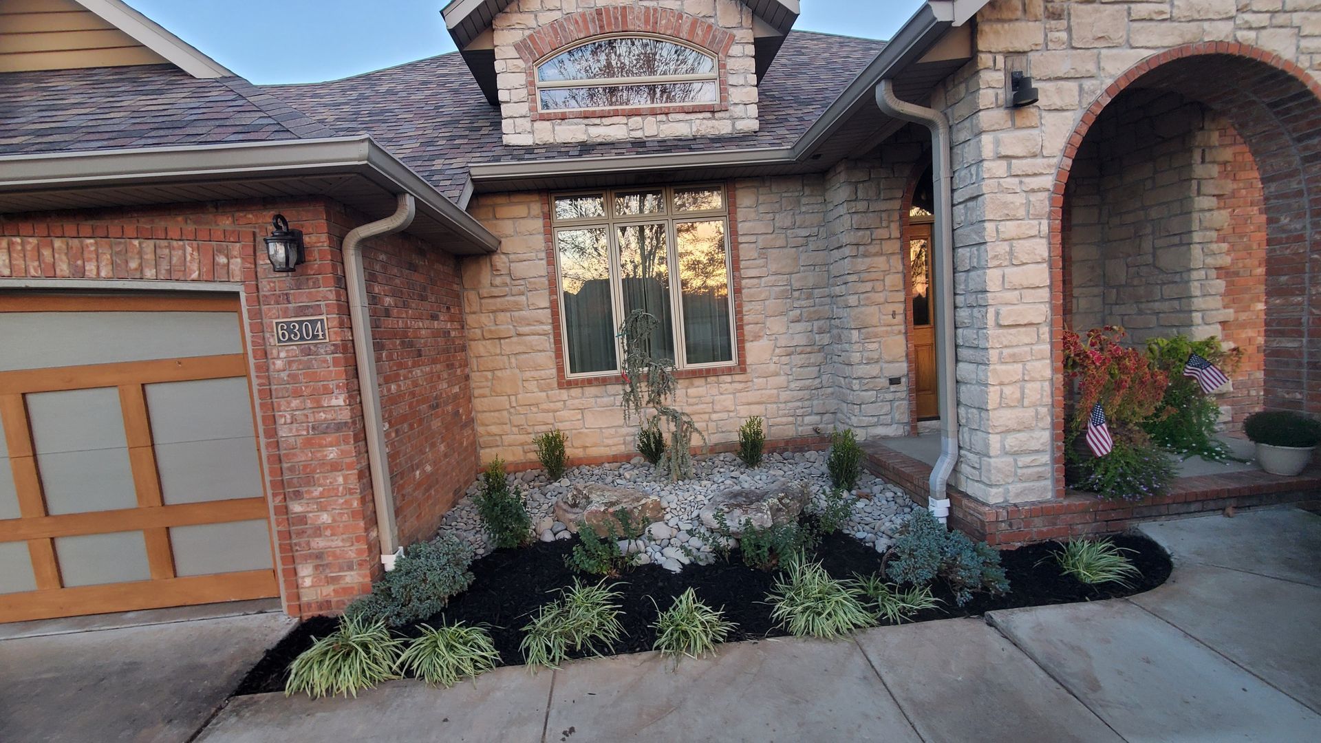 A brick house with a newly landscaped front yard, featuring mulch, rocks, and plants.