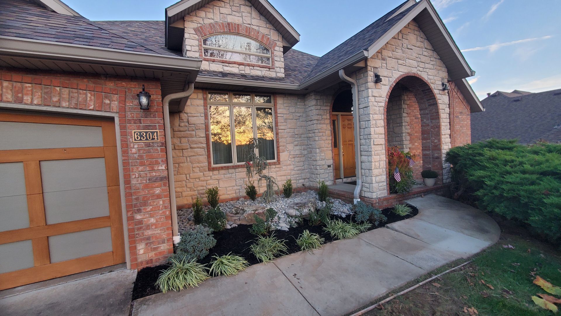 House exterior with brick and stone facade, wooden door, and landscaped garden.