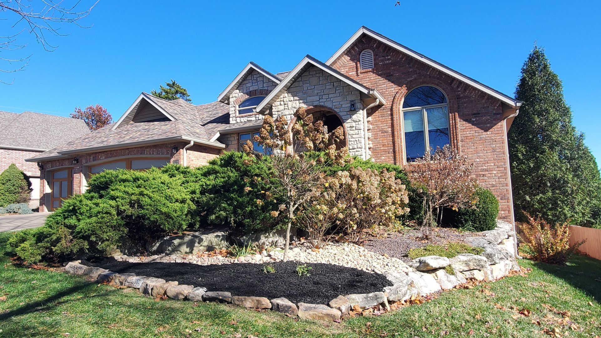 Two-story house with brick and stone facade, landscaped yard, blue sky.