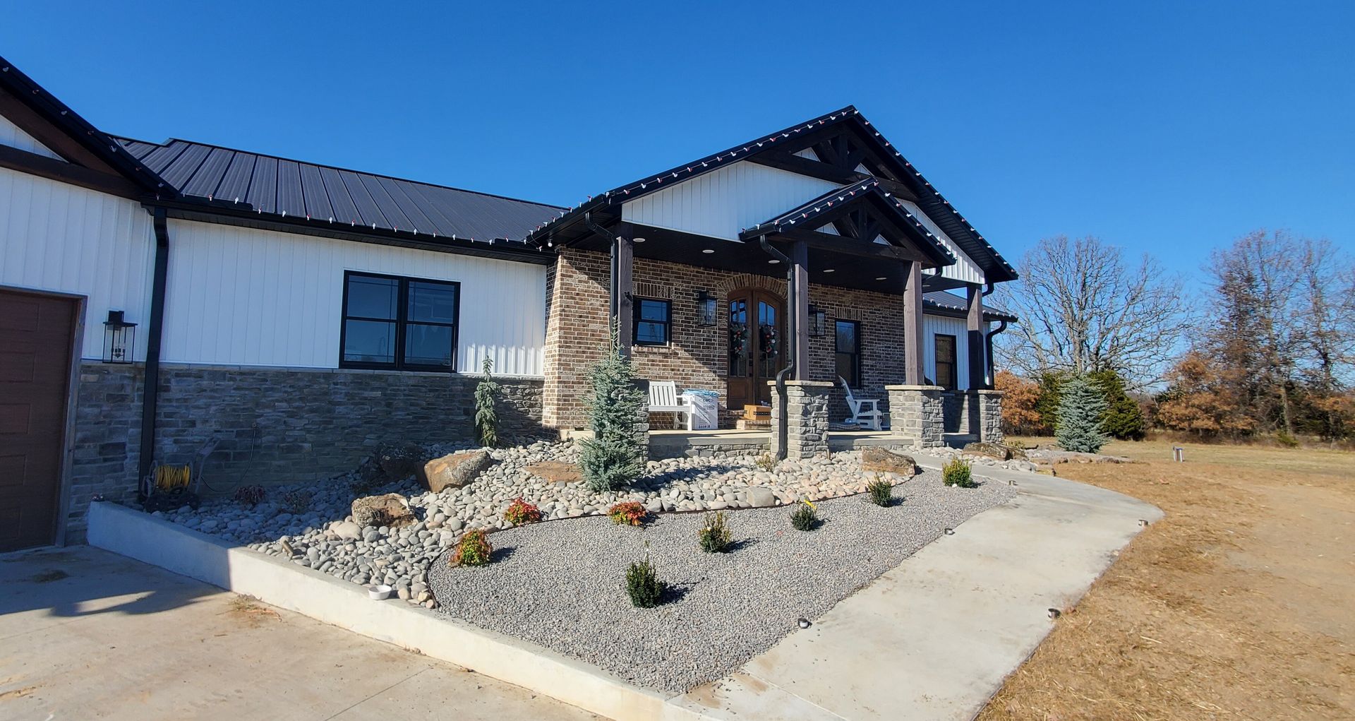 Modern house with white siding, stone accents, black roof and trim, and a gravel and rock landscaped yard.