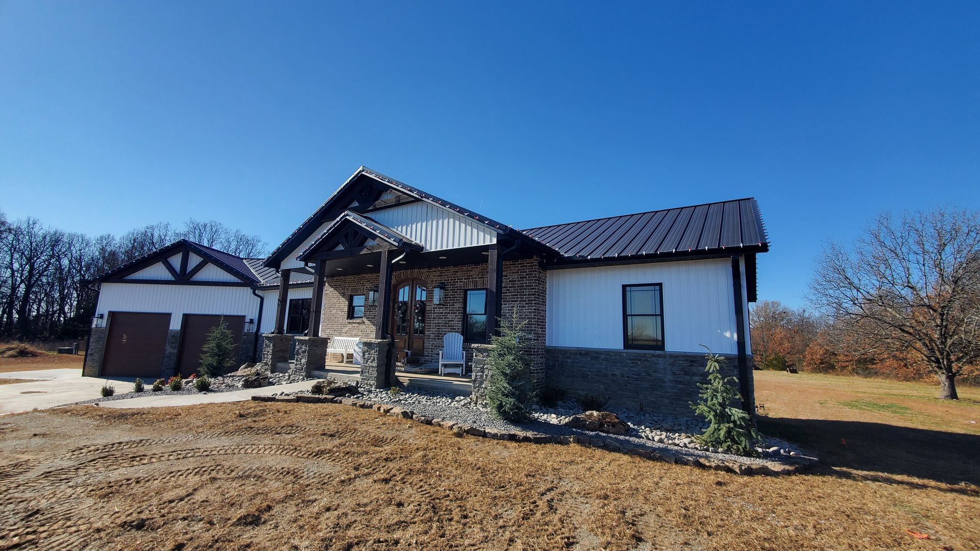 Modern farmhouse with white siding, stone accents, and black roof under a blue sky.