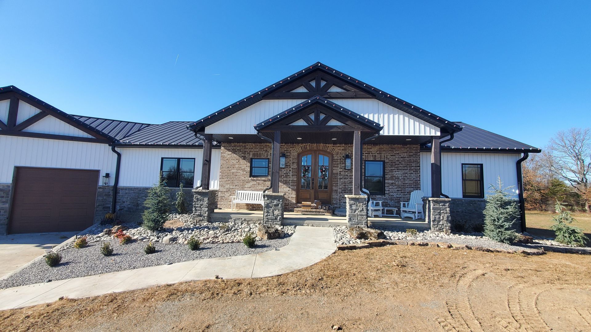 Modern farmhouse with white siding, stone accents, and brown trim on a sunny day.