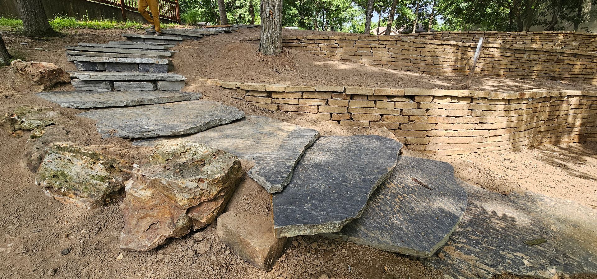 Stone steps and a low rock wall in a wooded outdoor park area