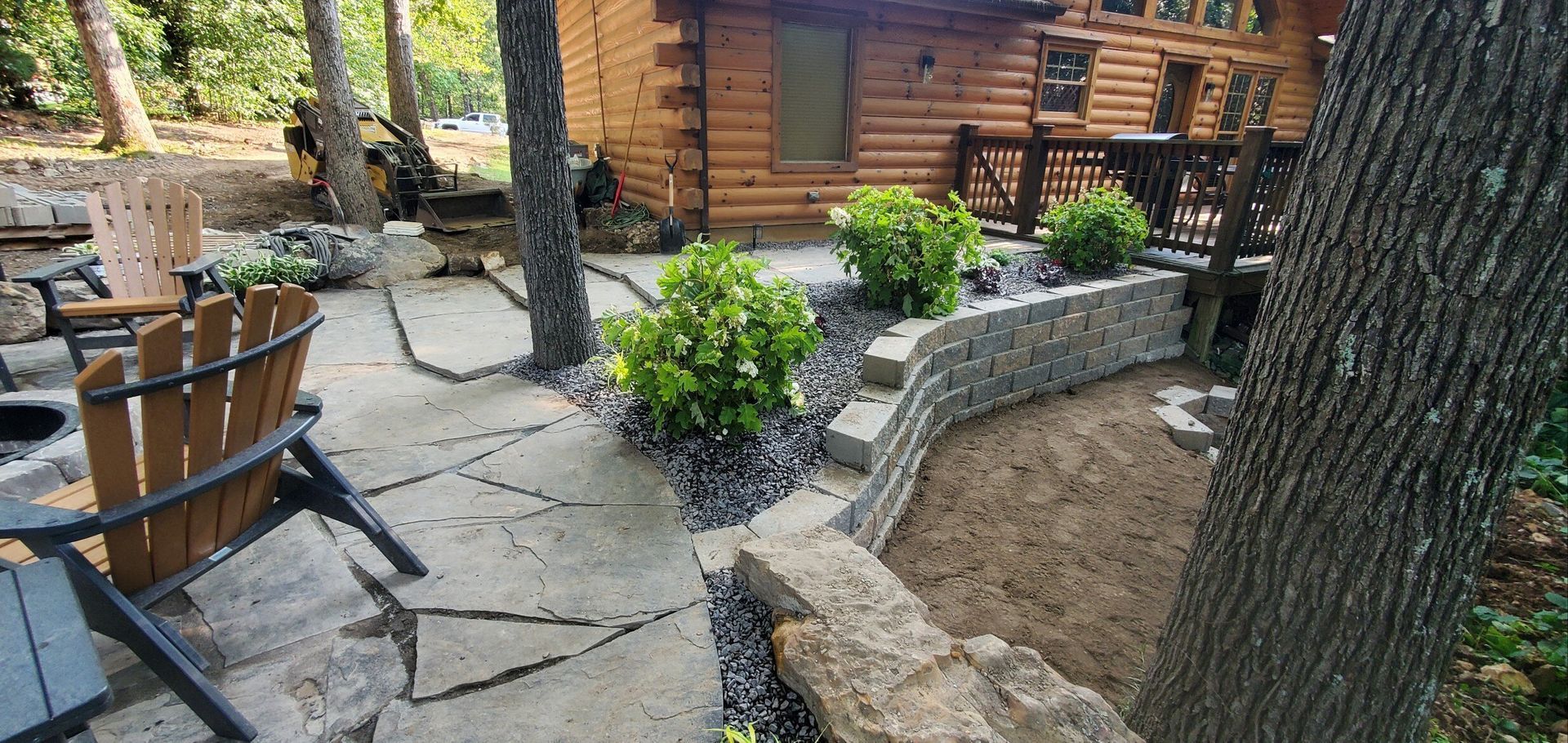 Patio with stone walkway, raised garden beds, log cabin, and Adirondack chairs.