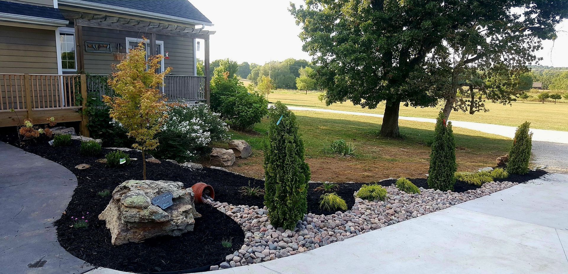 Landscaped front yard with house, trees, rocks, and mulch.