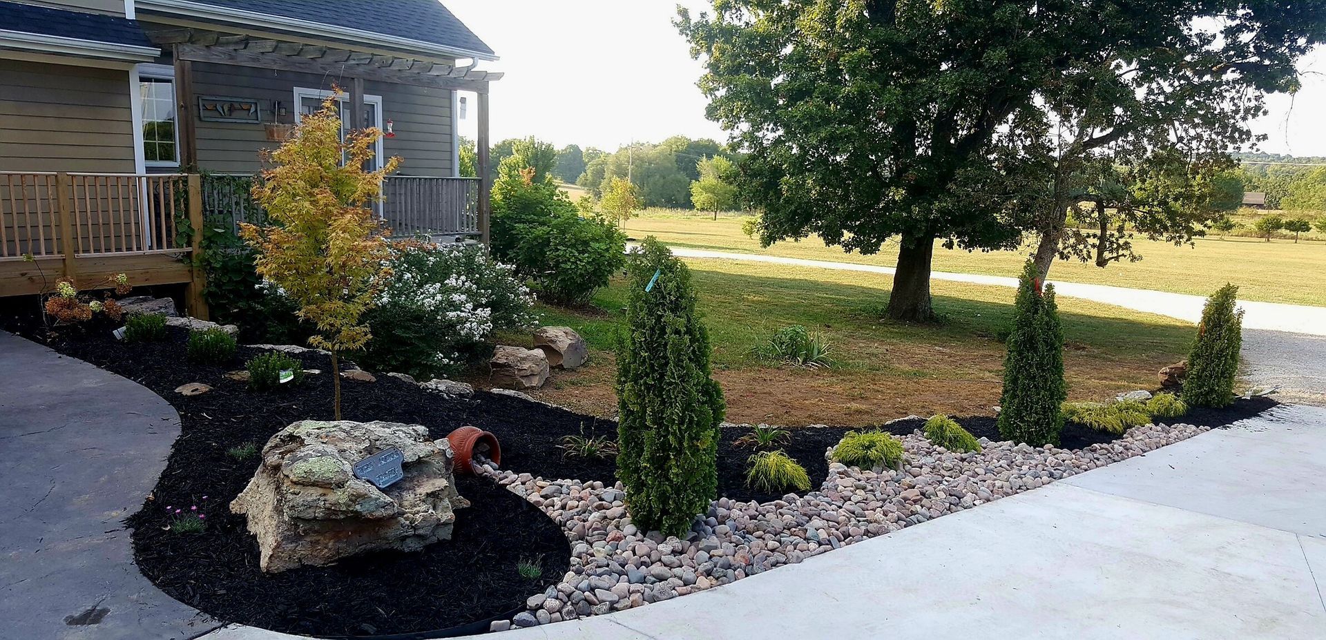 Landscaped yard with stone, trees, and mulch in front of a house.