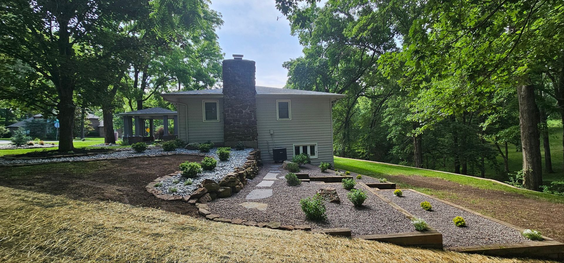 Landscaped yard with stone, trees, and mulch in front of a house.