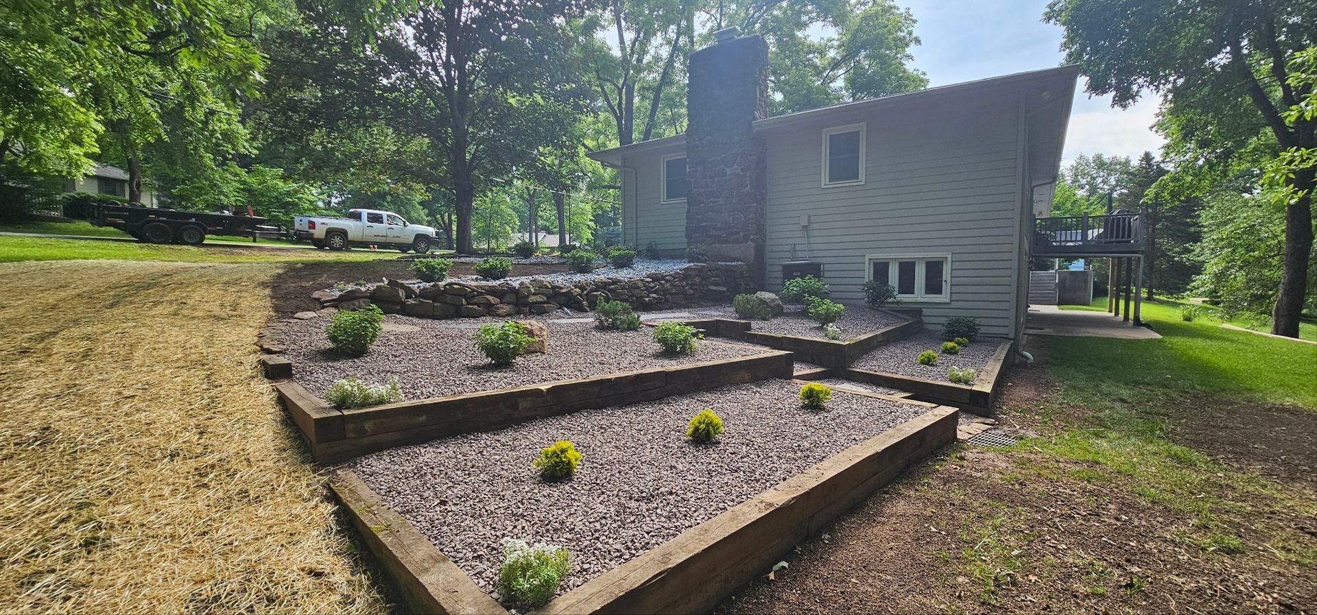 Landscaped yard with stone, trees, and mulch in front of a house.
