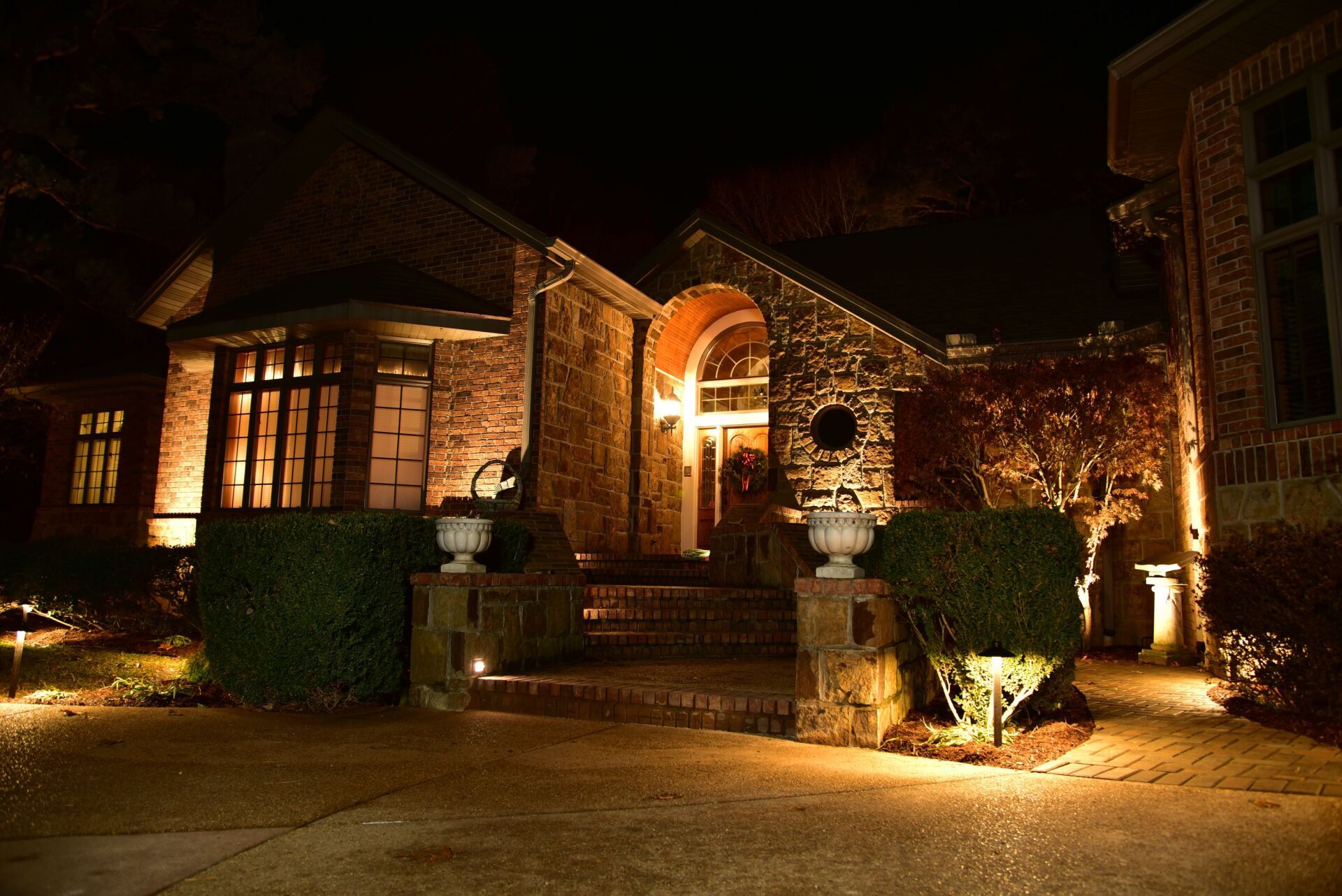 Night view of a house with warm exterior lighting, highlighting the brick facade, entrance, and landscaping.