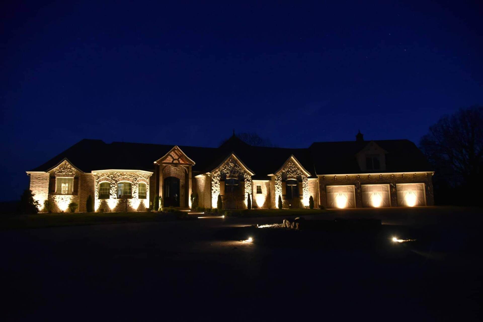 Illuminated house at night with spotlighting on stone facade and garage.