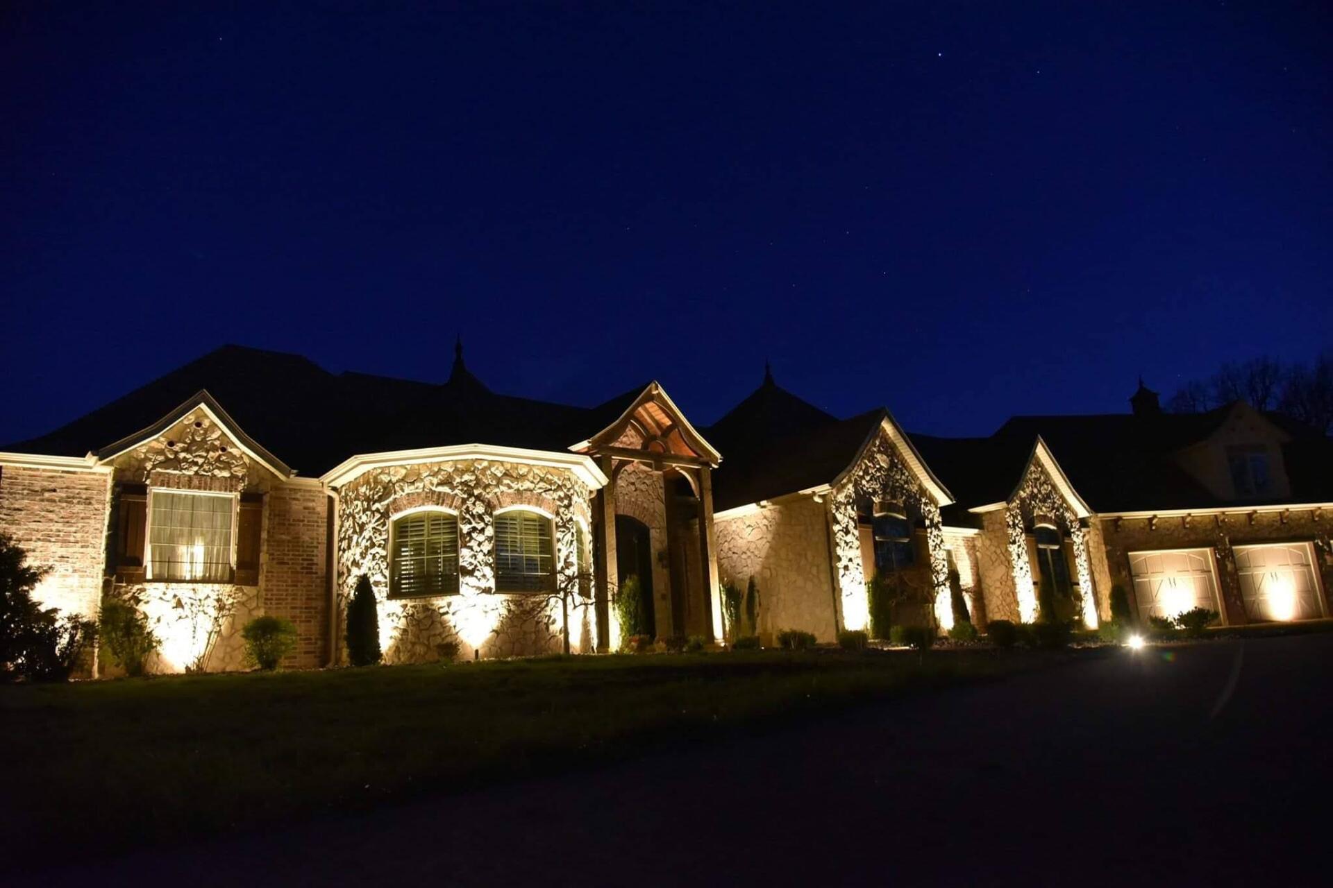 Night view of a large house illuminated by spotlights, showcasing stonework and architectural details.